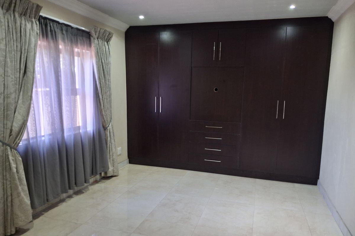 A spacious bedroom featuring large dark wood built-in cupboards, neutral tiled flooring, and recessed ceiling lighting.