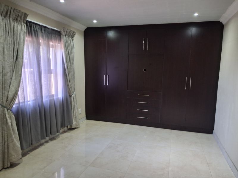 A spacious bedroom featuring large dark wood built-in cupboards, neutral tiled flooring, and recessed ceiling lighting.