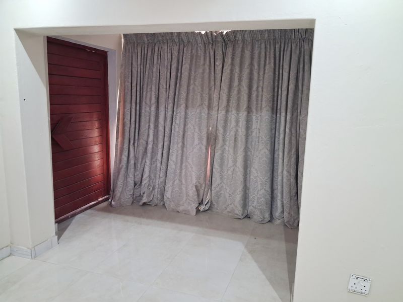 An empty living area featuring tiled flooring and a wooden door, providing a blank canvas for interior design.