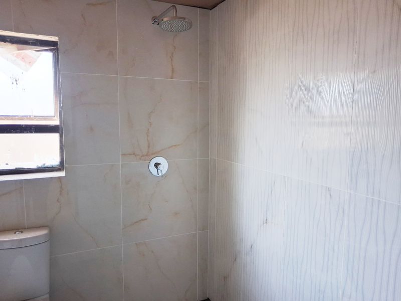 A modern bathroom featuring large format marble-look wall tiles, a rainfall shower head, and a sleek toilet.