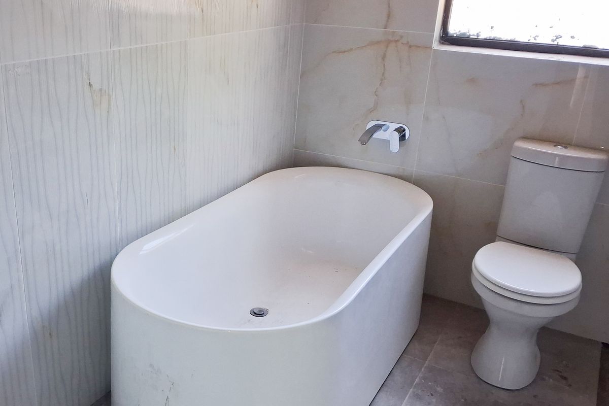 A modern bathroom featuring a freestanding bathtub, wall-mounted mixer, and a standard toilet with neutral wall and floor tiling.