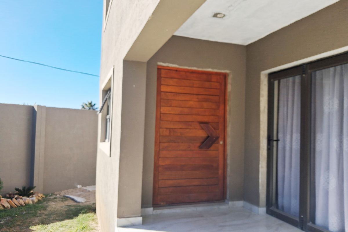 A rear exterior view of the apartment featuring a wooden entrance door, sliding glass doors, and a tiled patio area.