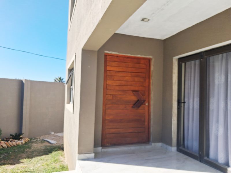 A rear exterior view of the apartment featuring a wooden entrance door, sliding glass doors, and a tiled patio area.