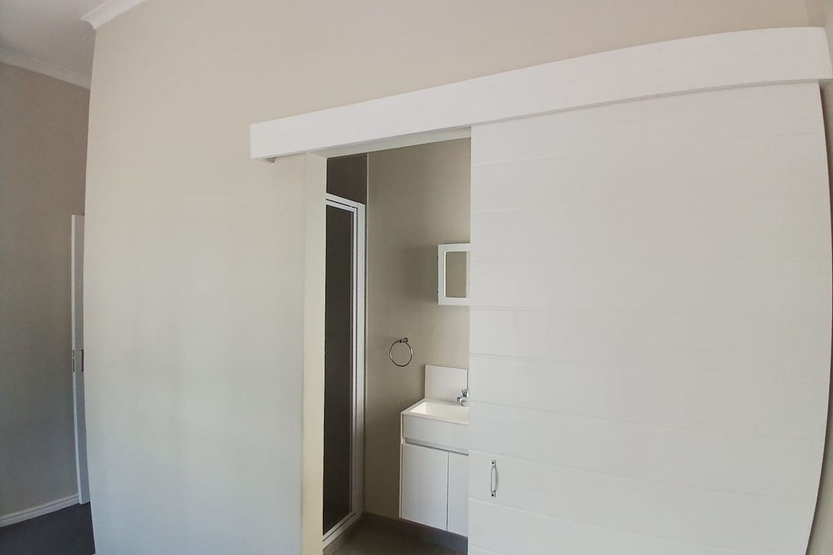 A view into a modern bathroom featuring a vanity with integrated sink, shower enclosure, and a white sliding barn-style door.