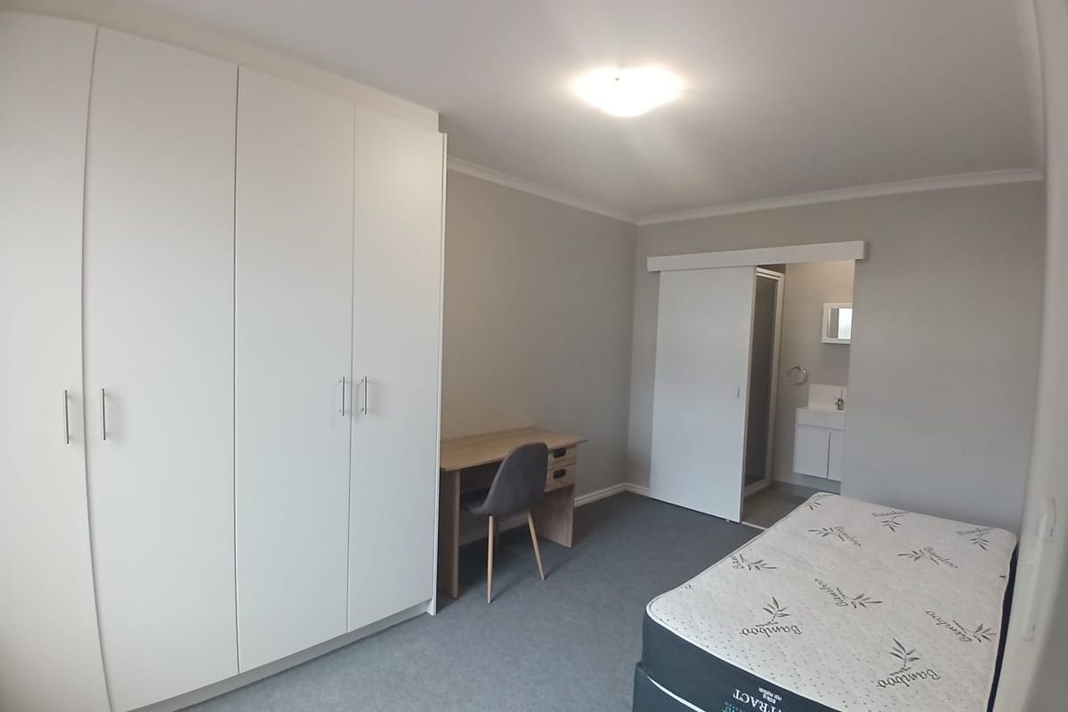 A well-maintained bedroom featuring built-in wardrobes, neutral carpeting, and an en-suite bathroom accessed via a sliding door.