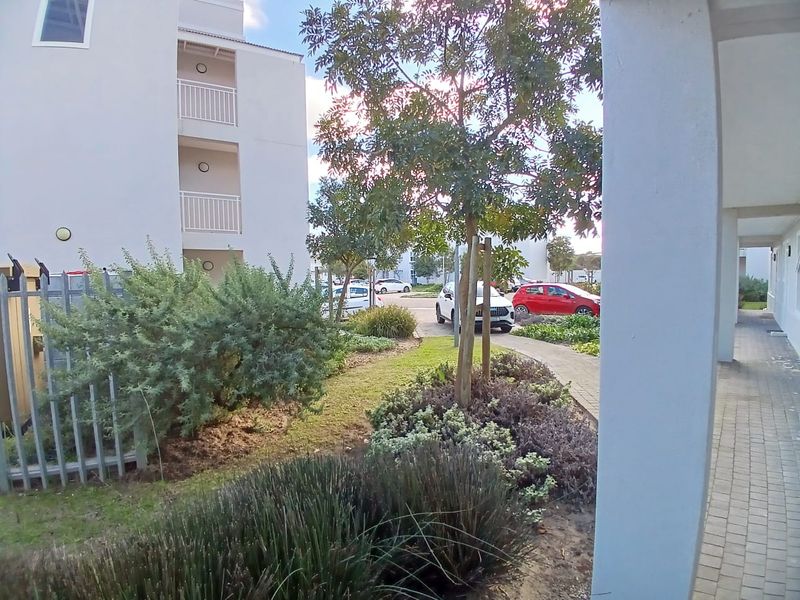 A view of the apartment complex exterior featuring a landscaped garden, paved walkways, and multi-level balconies.