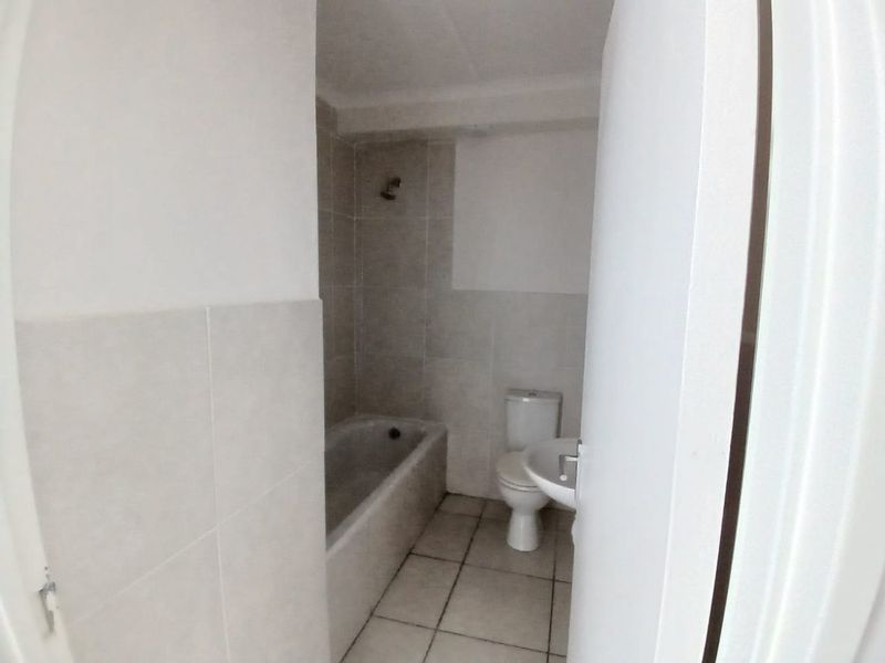 A functional bathroom featuring a bathtub with shower head, a standard toilet, and a pedestal basin with neutral wall and floor tiling.