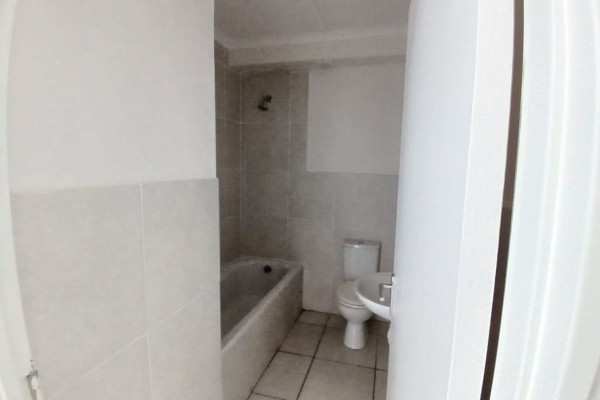 A functional bathroom featuring a bathtub with shower head, a standard toilet, and a pedestal basin with neutral wall and floor tiling.