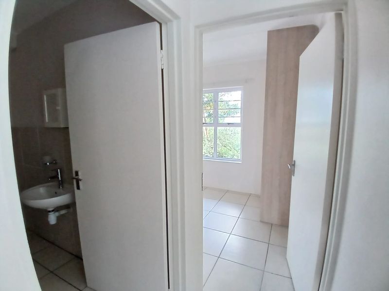 A view from the hallway looking into a bedroom and a bathroom, featuring tiled floors and a built-in cupboard.