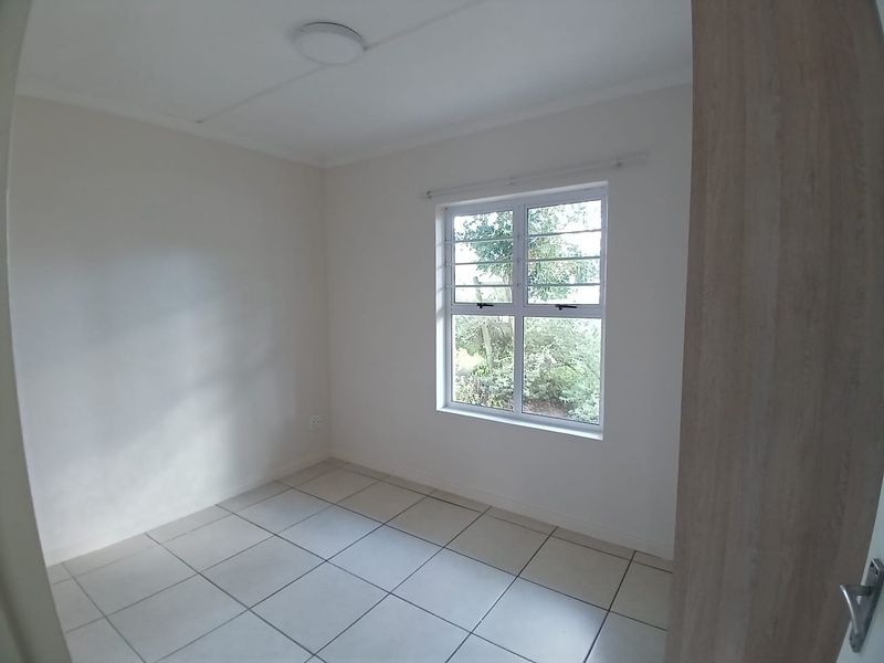 A clean, empty bedroom featuring neutral tiled flooring, a window with security bars, and a simple ceiling light fixture.