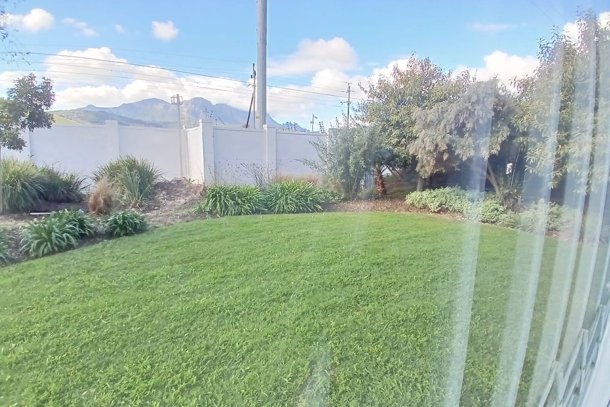 A well-maintained private garden featuring a lush green lawn, perimeter wall with electric fencing, and established shrubbery with mountain views in the background.
