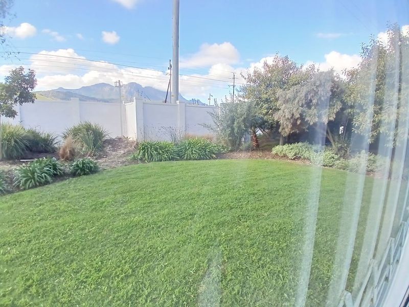 A well-maintained private garden featuring a lush green lawn, perimeter wall with electric fencing, and established shrubbery with mountain views in the background.