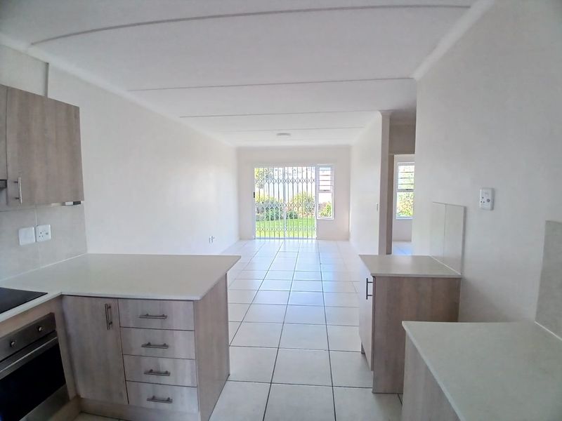 Bright open-plan living area featuring a modern kitchen with built-in cabinetry and oven, leading to a tiled lounge with access to the garden.