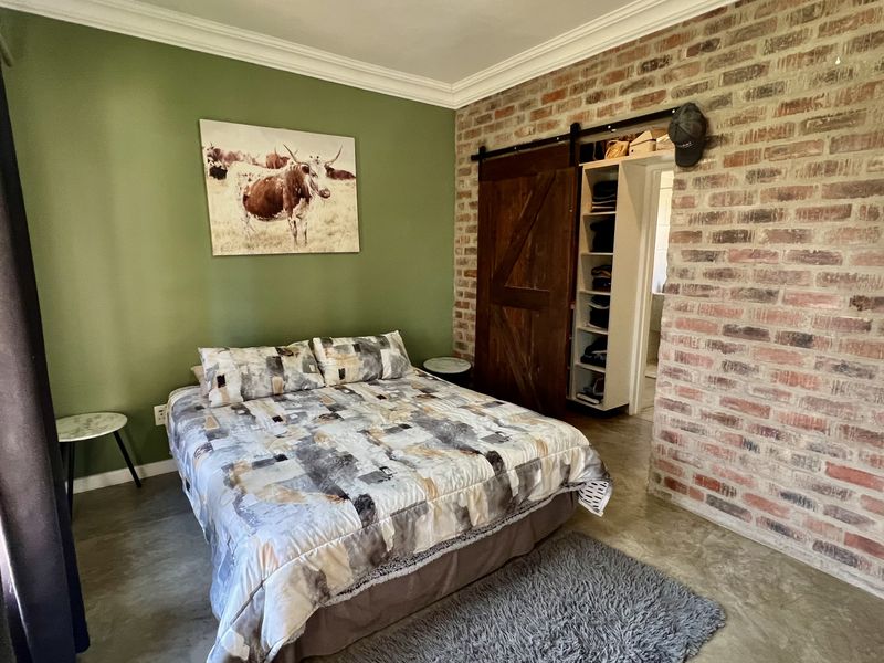 A well-maintained bedroom featuring an exposed brick feature wall, polished concrete floors, crown molding, and a sliding barn door leading to built-in storage.