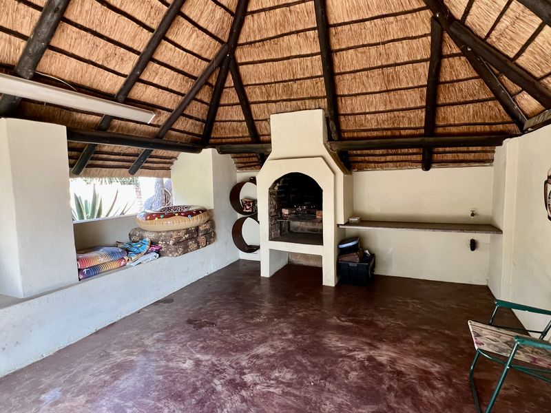 Covered outdoor entertainment area featuring a traditional thatched roof, built-in braai, and integrated concrete bench seating, ideal for alfresco dining and social gatherings.