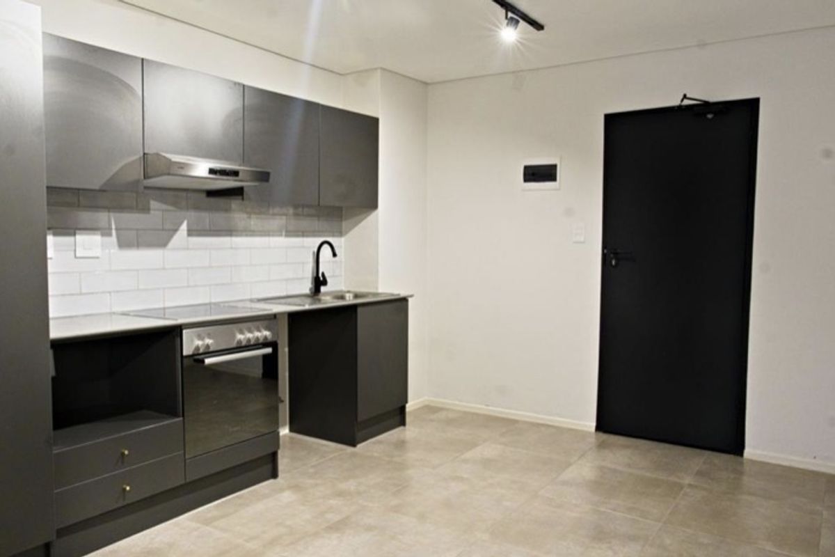Modern kitchen featuring dark grey cabinetry, subway tile backsplash, integrated oven and hob, and neutral tiled flooring in a clean, minimalist space.