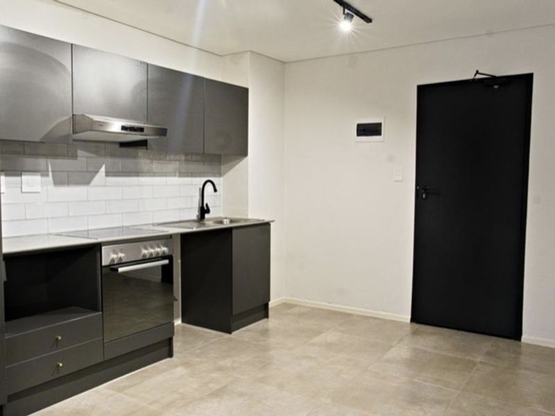 Modern kitchen featuring dark grey cabinetry, subway tile backsplash, integrated oven and hob, and neutral tiled flooring in a clean, minimalist space.