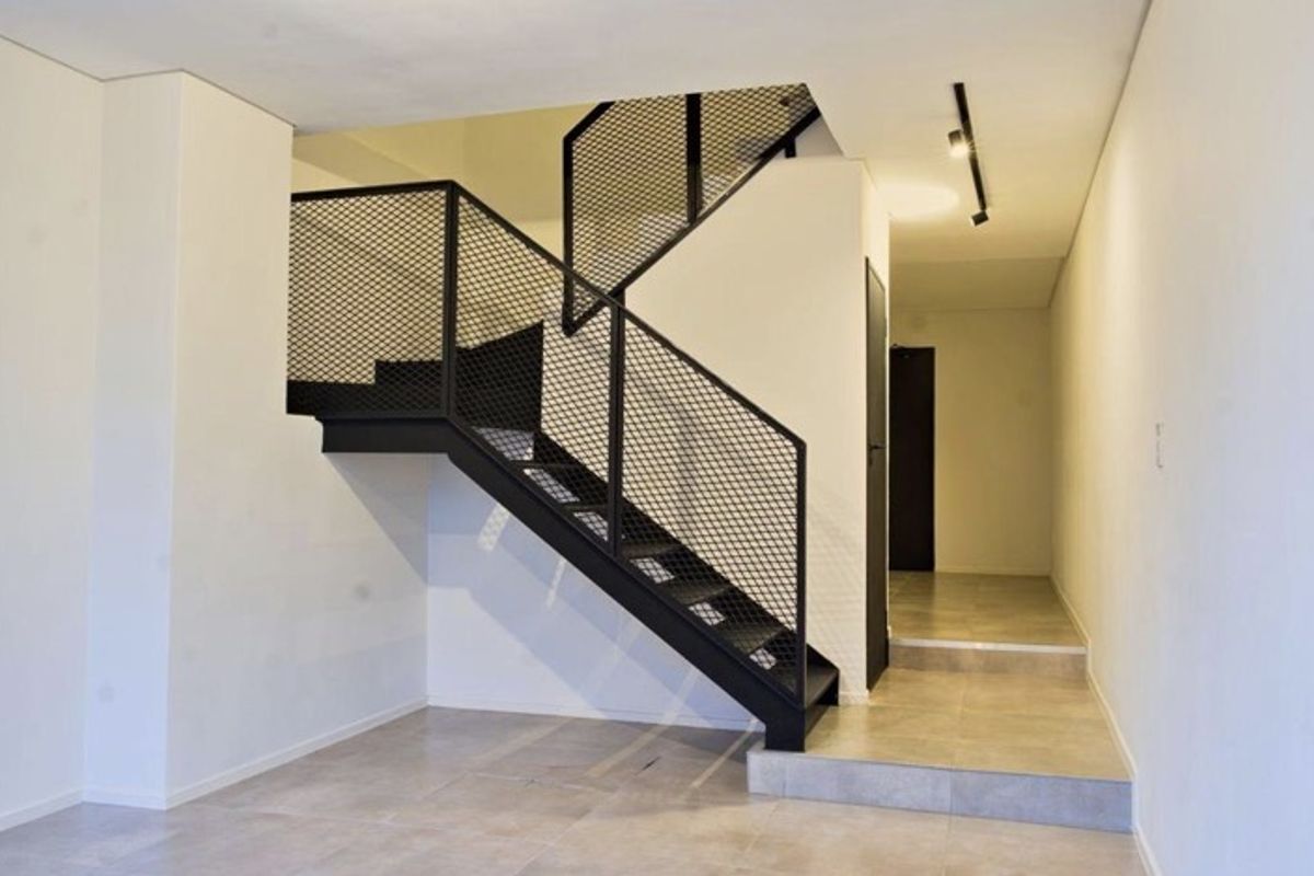 Modern interior hallway featuring a striking black metal staircase with mesh balustrade, tiled flooring, and minimalist track lighting.
