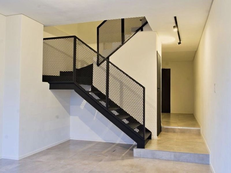 Modern interior hallway featuring a striking black metal staircase with mesh balustrade, tiled flooring, and minimalist track lighting.