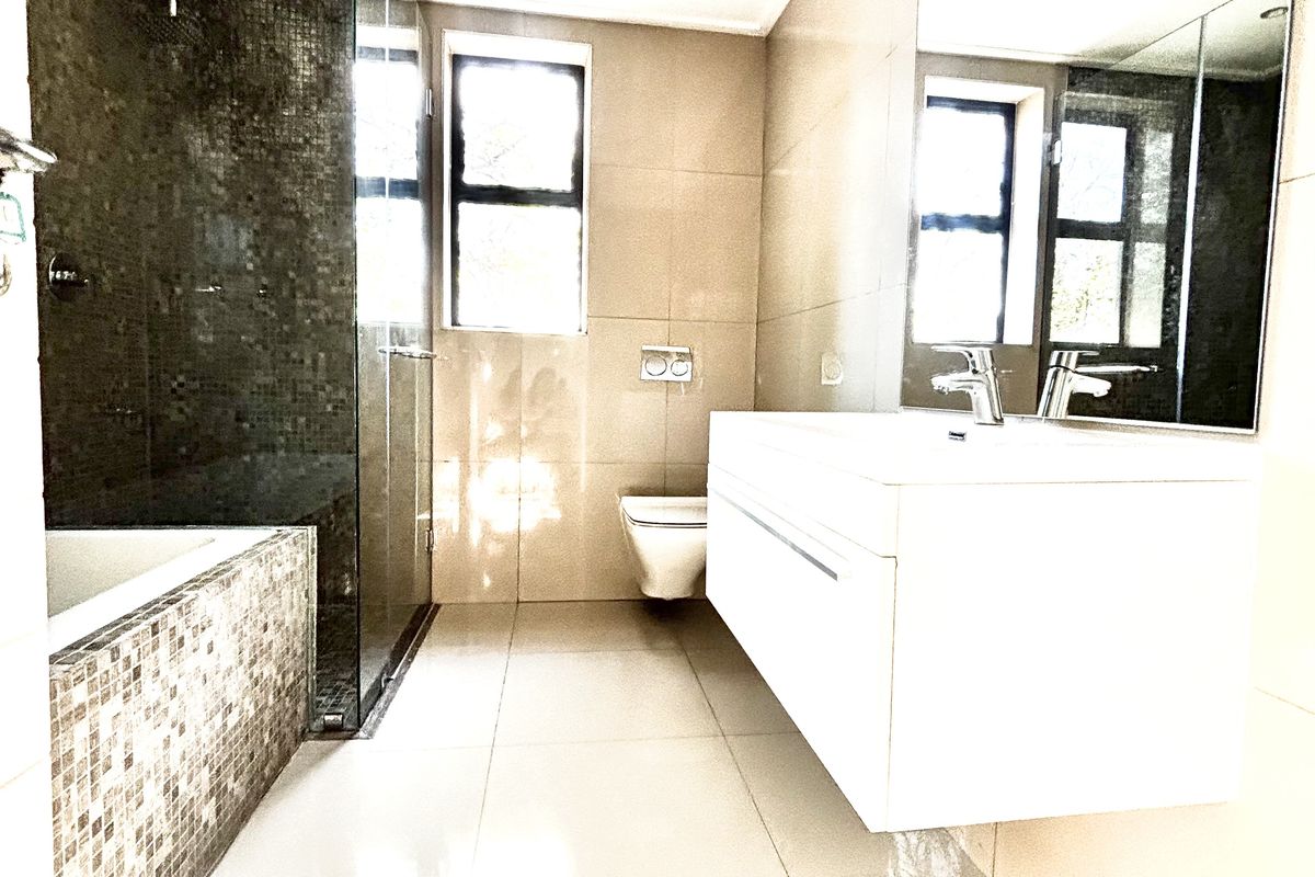 Modern bathroom featuring a floating vanity, large wall-mounted mirror, glass-enclosed shower, and a tiled bathtub with mosaic accents.