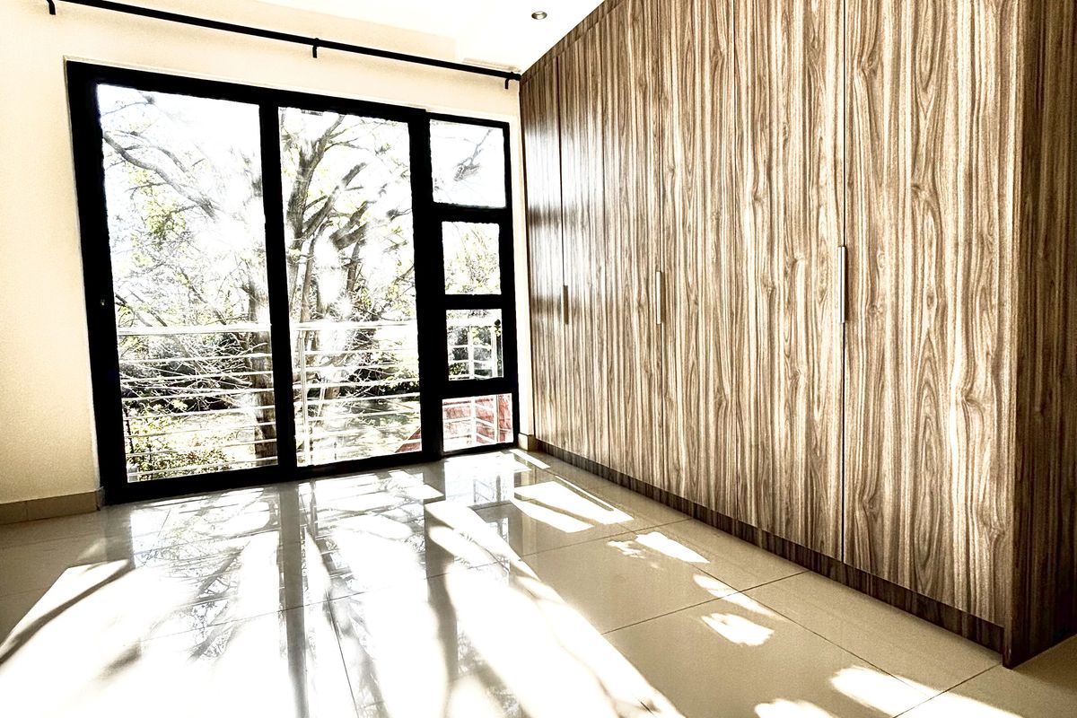 A bright bedroom featuring large floor-to-ceiling built-in wooden wardrobes, tiled flooring, and a sliding glass door leading to an outdoor balcony.