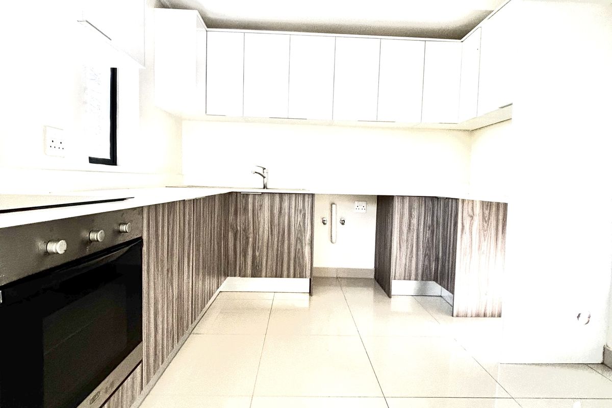 Modern kitchen featuring sleek wood-grain cabinetry, white countertops, integrated oven, and polished floor tiles in a bright, open-plan layout.