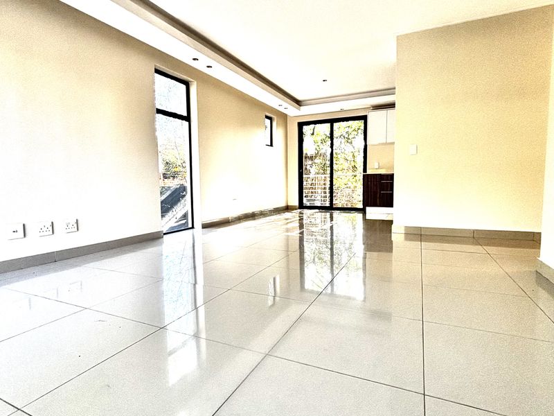 A bright, open-plan living area featuring polished porcelain floor tiles, recessed ceiling lighting, and large glass sliding doors leading to an outdoor space.