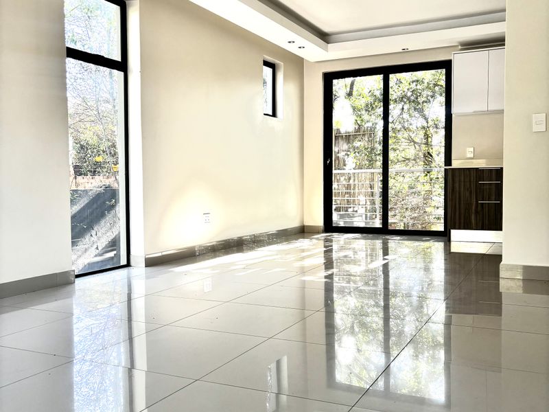 Bright open-plan living area featuring polished porcelain floor tiles, recessed ceiling lighting, and large glass sliding doors leading to an outdoor space.