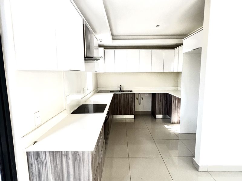 Modern kitchen featuring sleek two-tone cabinetry, integrated cooktop, stainless steel sink, and polished floor tiles in an open-plan layout.