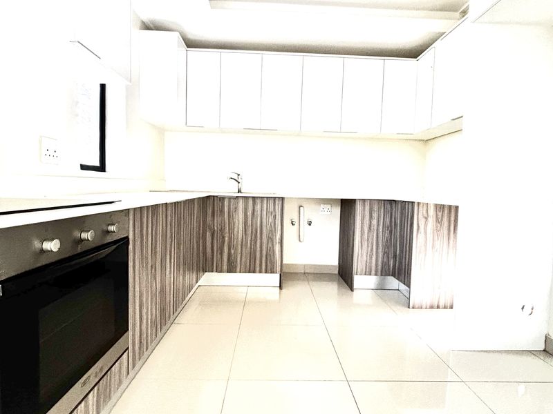 Modern kitchen featuring sleek wood-grain cabinetry, white countertops, integrated oven, and polished floor tiles in a bright, open-plan layout.