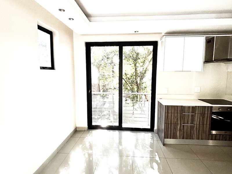 Modern open-plan kitchen featuring sleek cabinetry, built-in oven, hob, and extractor fan, with large sliding doors leading to a balcony.