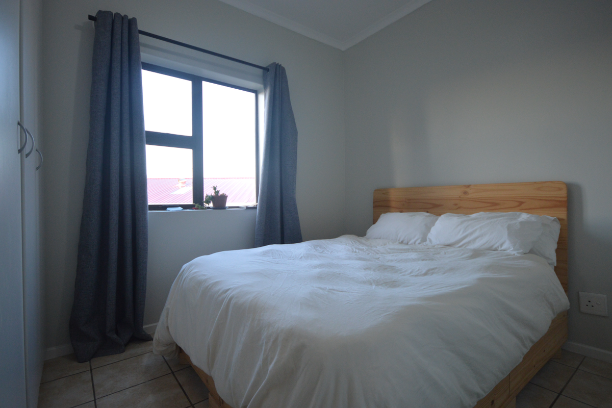 A well-maintained bedroom featuring neutral wall tones, tiled flooring, and a large window that allows for natural light.