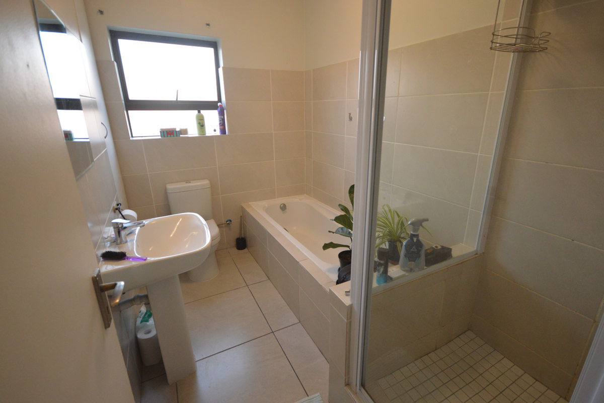 A functional bathroom featuring a pedestal basin, a built-in bathtub, and a separate shower enclosure with glass screen and tiled walls.