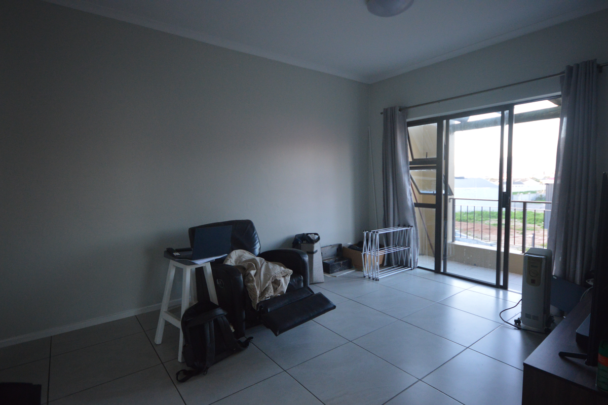 A living room featuring large format floor tiles and sliding glass doors that provide access to an outdoor balcony area.