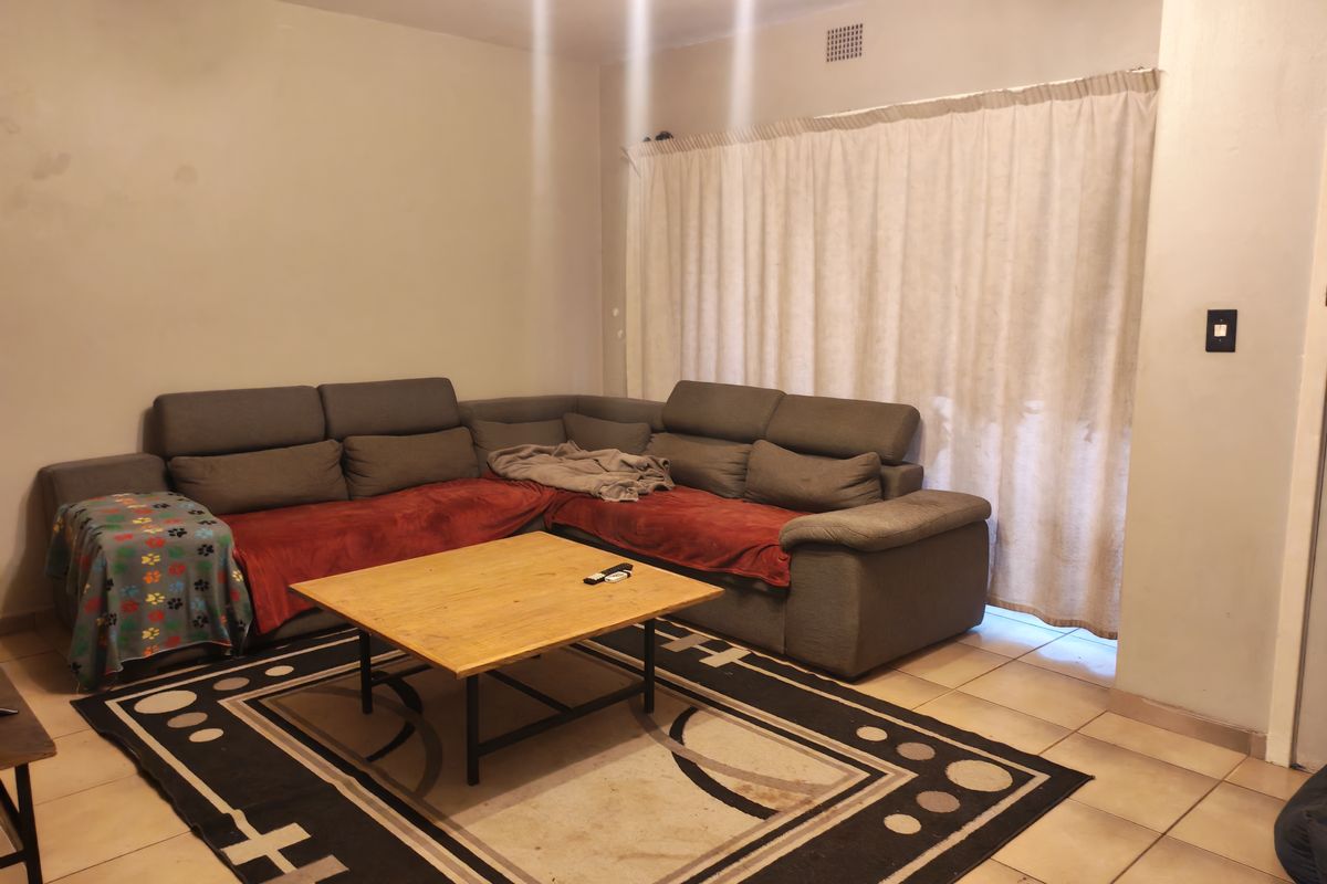 A living room featuring tiled flooring and a large window covered by curtains, providing a functional space for relaxation.