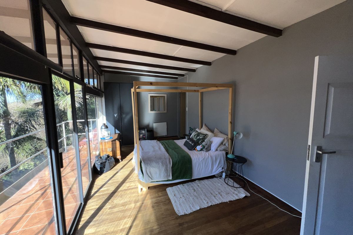 Spacious bedroom featuring exposed timber ceiling beams, hardwood flooring, and large sliding glass doors opening onto a private balcony.