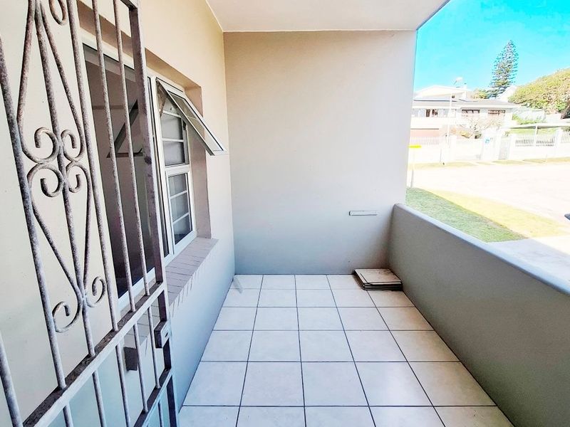 A clean, covered balcony featuring tiled flooring, a secure metal gate, and a casement window, offering a functional outdoor space.