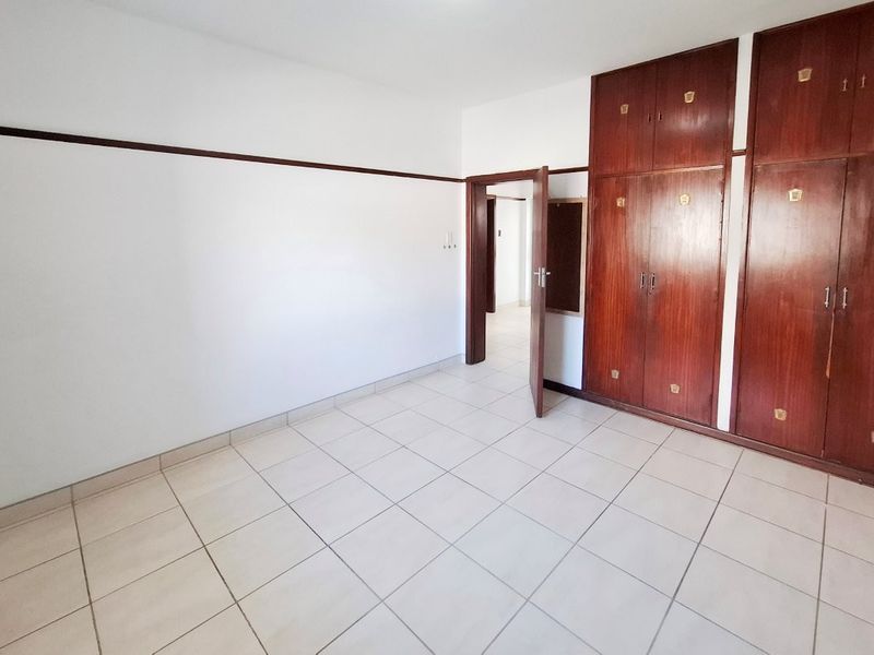 An empty bedroom featuring tiled flooring and extensive built-in wooden cabinetry, offering a blank canvas for personalization.