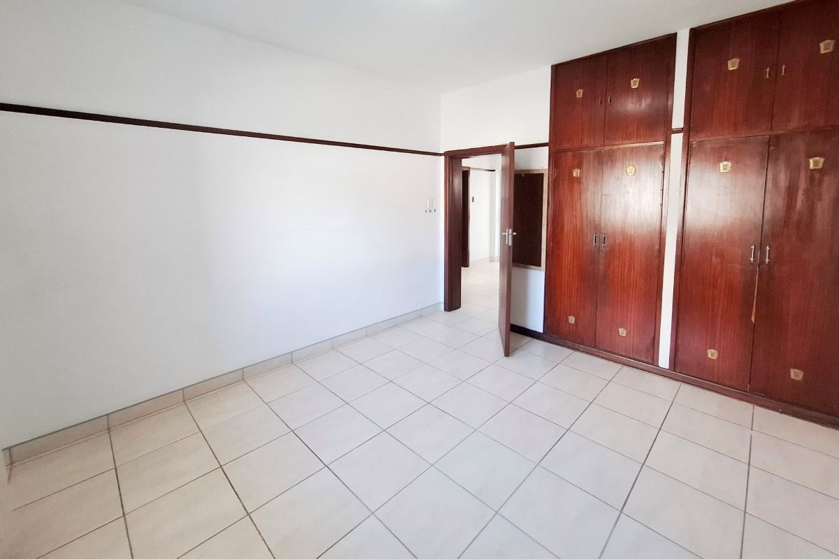 An empty bedroom featuring tiled flooring and extensive built-in wooden cabinetry, offering a blank canvas for personalization.