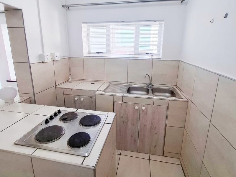 A functional kitchen featuring a built-in hob, double sink, tiled splashbacks, and neutral floor tiles, offering a clean and practical workspace.