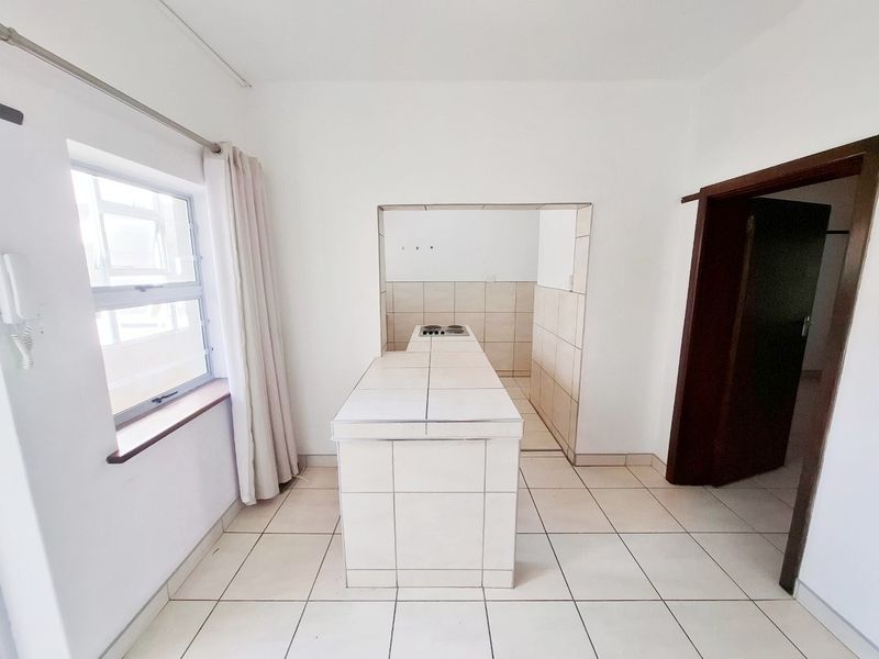 A functional kitchen area featuring a tiled island with a built-in hob, tiled splashbacks, and neutral floor tiles in an open-plan layout.