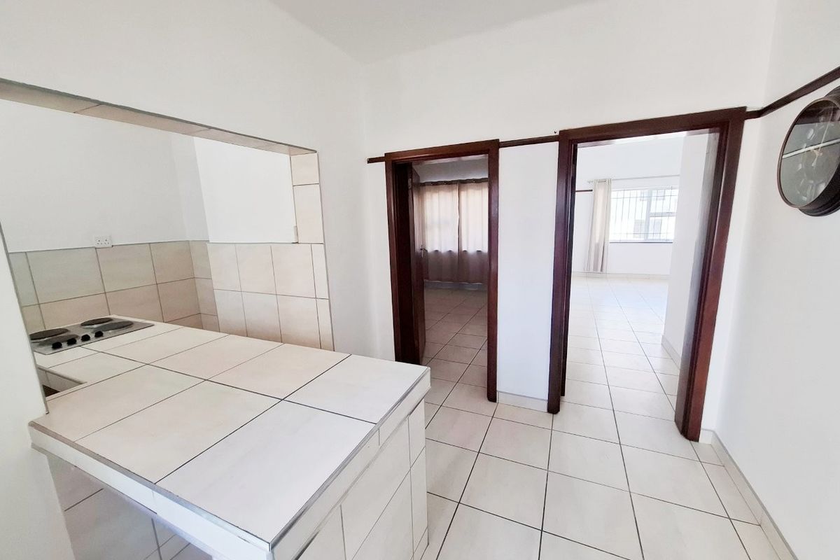 A functional kitchen area featuring a tiled counter with a built-in hob, leading into adjacent living spaces through wooden door frames.