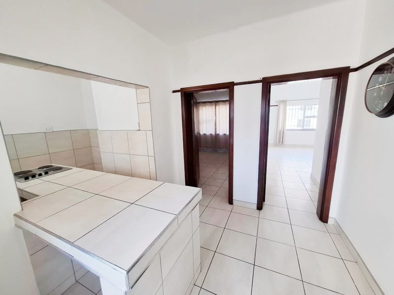 A functional kitchen area featuring a tiled counter with a built-in hob, leading into adjacent living spaces through wooden door frames.