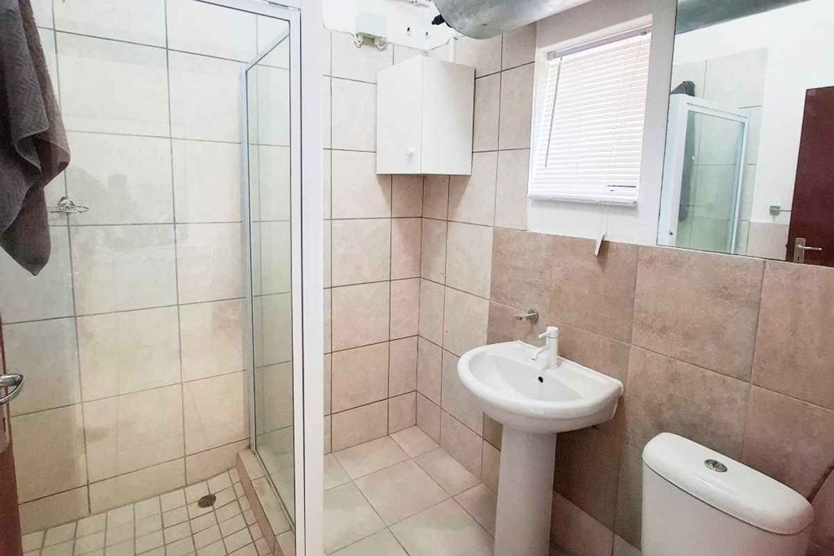 A functional bathroom featuring a glass shower enclosure, pedestal basin, and toilet, with visible exposed water heater infrastructure.