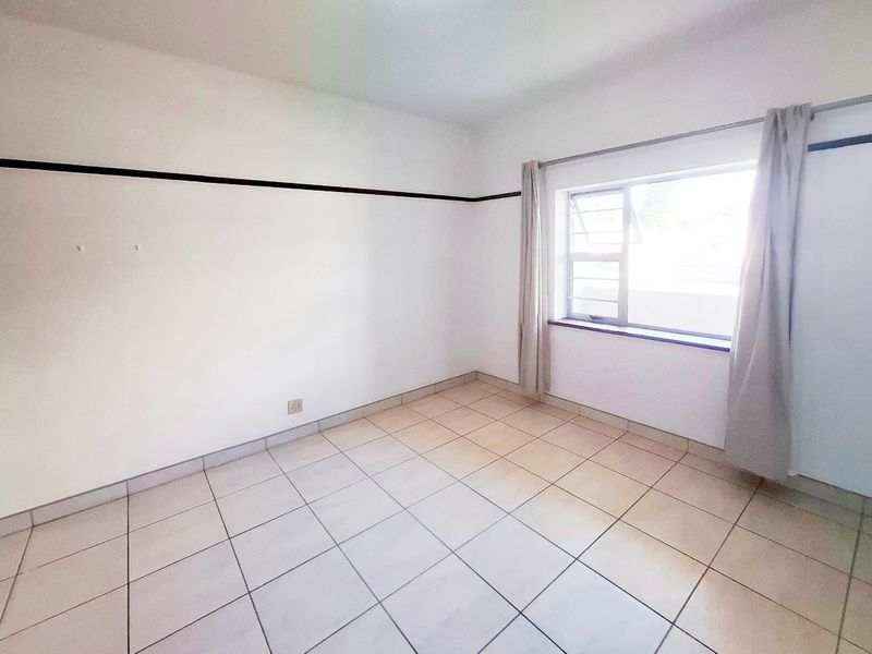 A vacant bedroom featuring neutral tiled flooring, a metal-framed window, and simple wall detailing, offering a clean canvas for personalization.