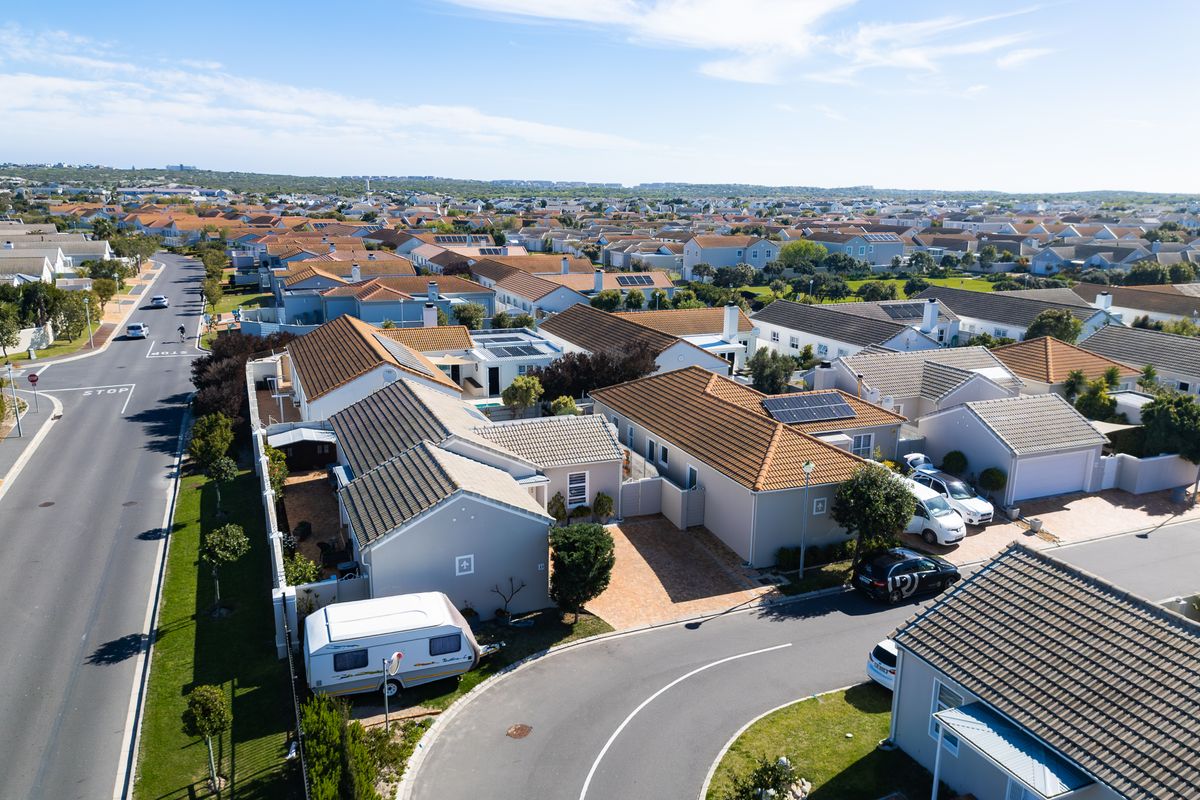 An aerial view of a residential neighborhood featuring multiple houses with tiled roofs, solar panels, and paved driveways in a suburban setting.