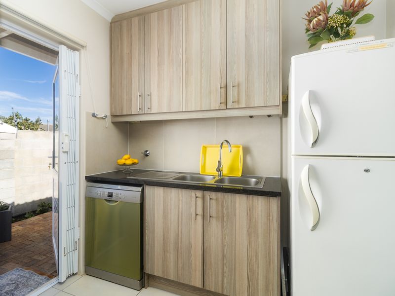 Compact scullery area featuring wood-look cabinetry, a stainless steel sink, and direct access to the outdoor patio area.