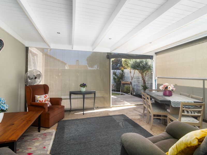 A covered patio area featuring an exposed beam ceiling, recessed lighting, and retractable outdoor blinds, providing a versatile space for outdoor living and dining.