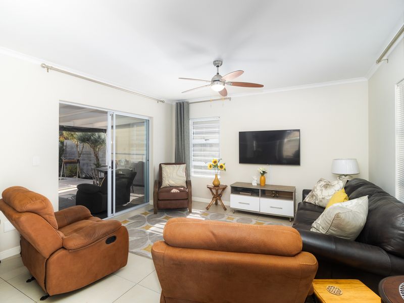 A bright living room featuring tiled flooring, a ceiling fan, and large sliding glass doors that provide direct access to the outdoor patio area.