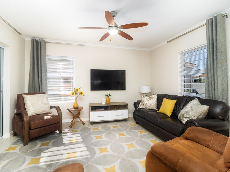A well-lit living room featuring tiled flooring, a ceiling fan, and sliding glass doors providing access to the outdoor area.